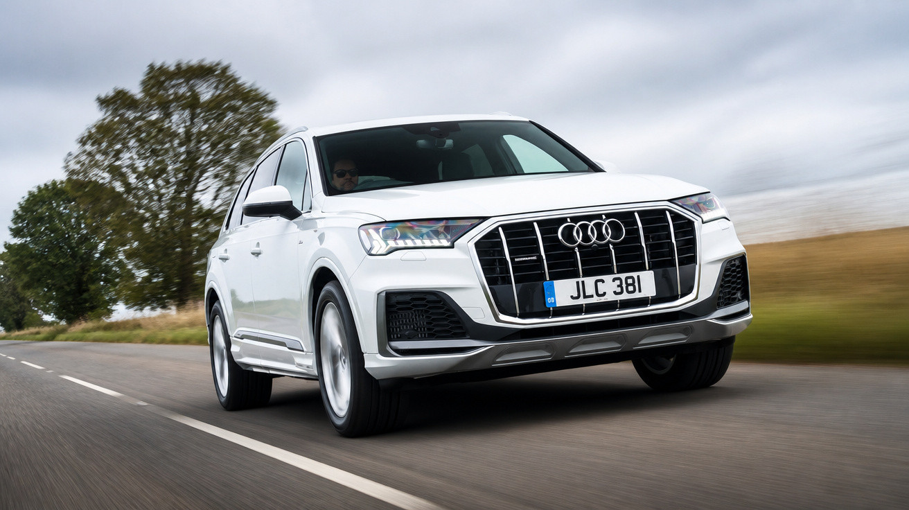 Weißer Audi Q7 fährt auf einer Landstraße bei bewölktem Himmel.