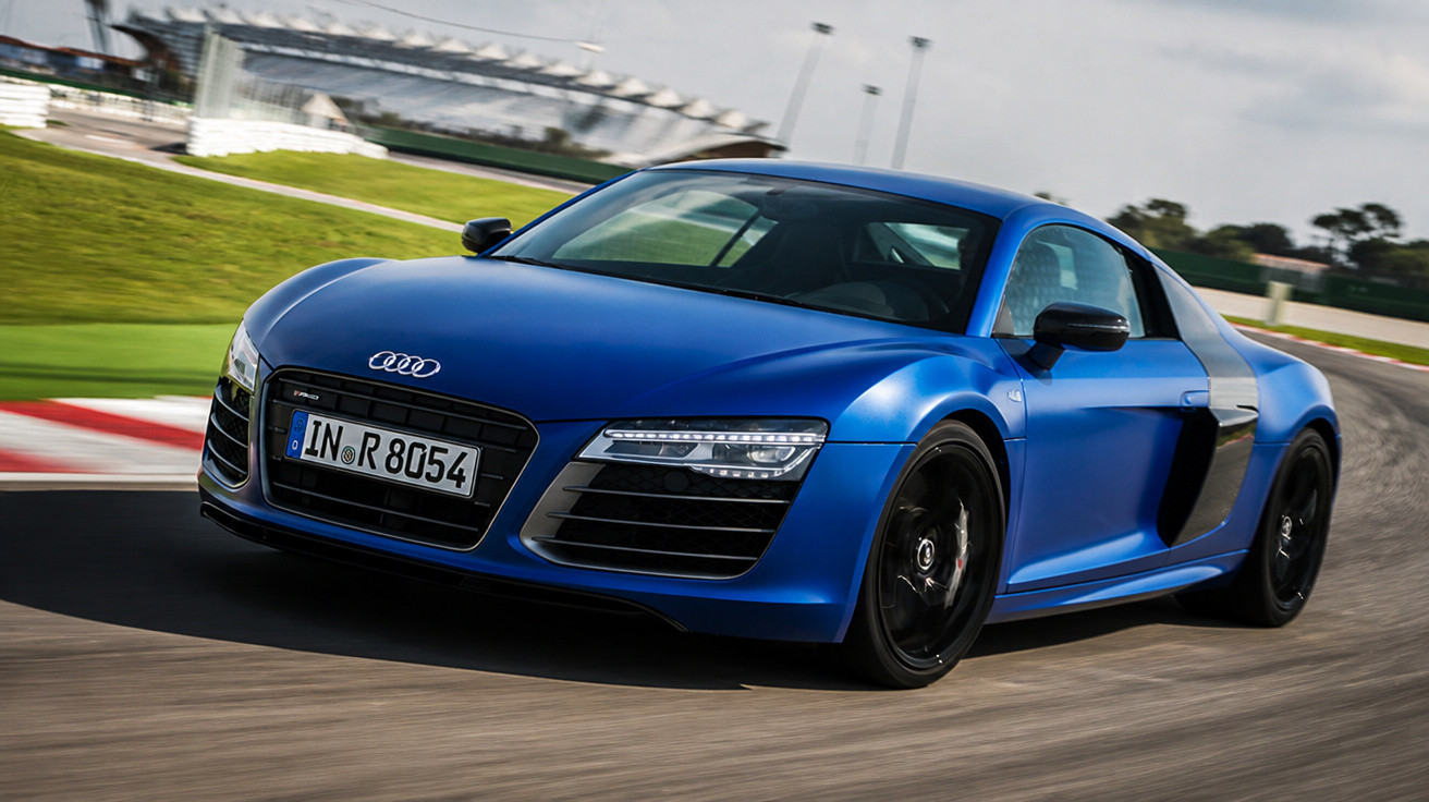 Blauer Audi R8 Sportwagen fährt auf Rennstrecke, dynamische Kurvenfahrt bei Tageslicht.