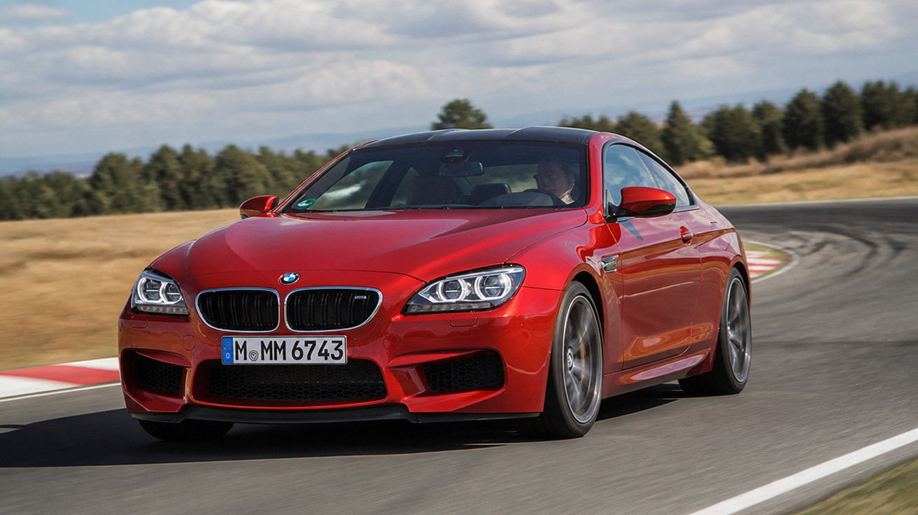 Roter BMW Sportwagen fährt auf einer kurvigen Rennstrecke bei klarem Himmel und trockenem Wetter.