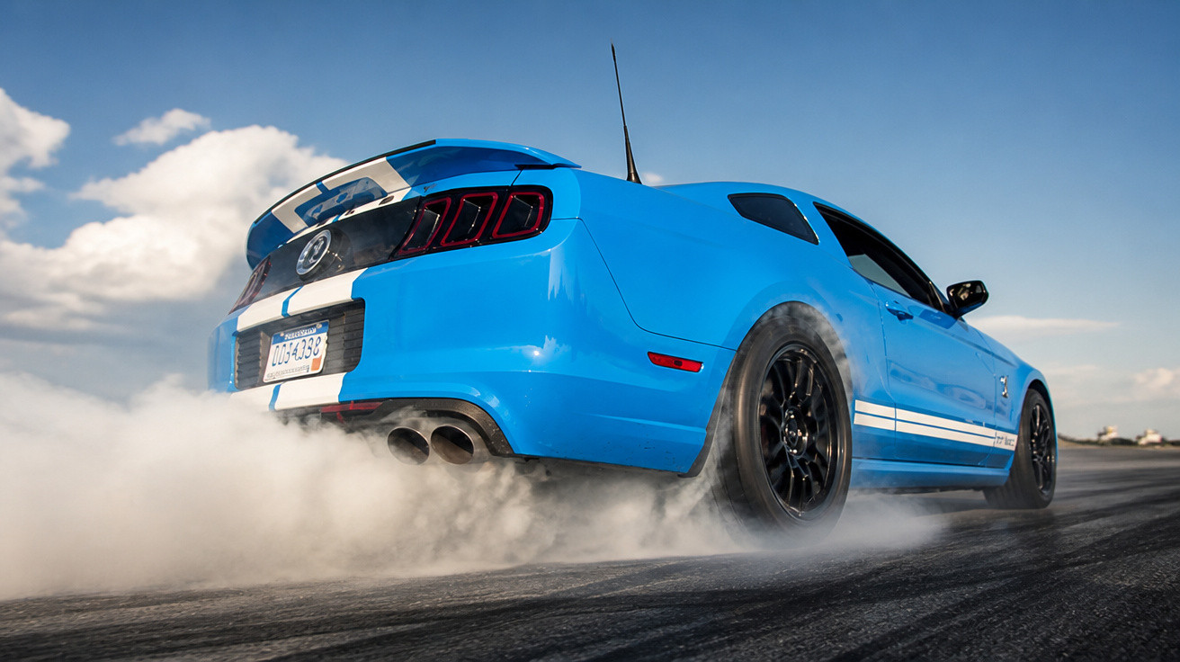 Blauer Sportwagen bei Burnout, Rauch steigen von den Reifen, blauer Himmel im Hintergrund.