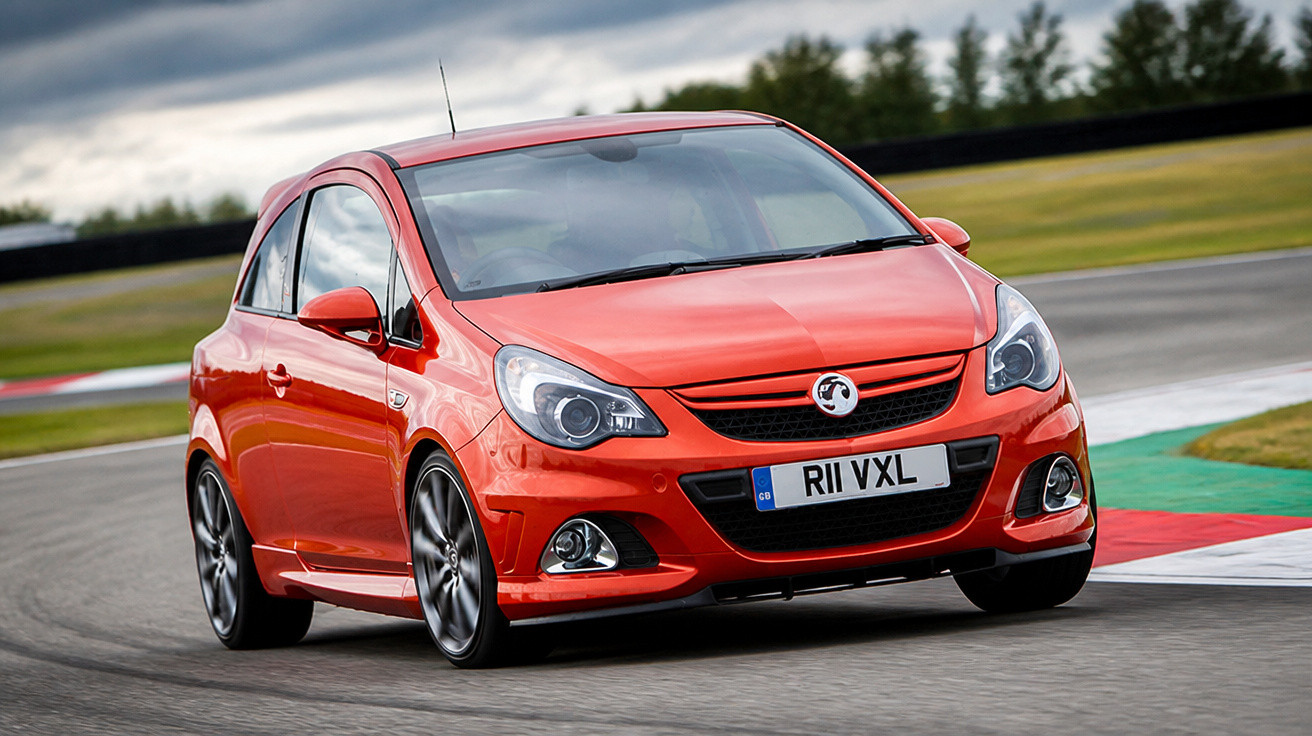 Roter Vauxhall Kleinwagen fährt schnell auf einer Rennstrecke bei bewölktem Himmel.