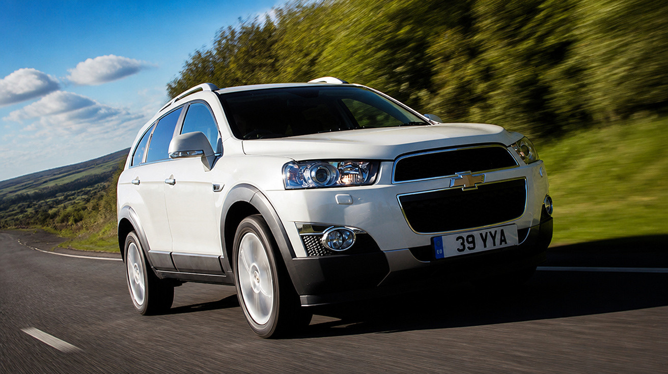 Weißer Chevrolet SUV fährt auf einer Landstraße bei sonnigem Wetter mit grünem Bewuchs im Hintergrund.