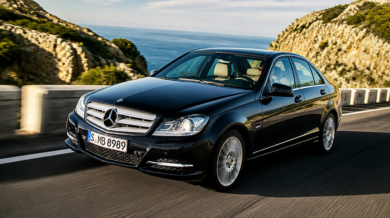 Schwarzer Mercedes-Benz auf Küstenstraße zwischen Felsen und Meer bei Sonnenschein fahrend.
