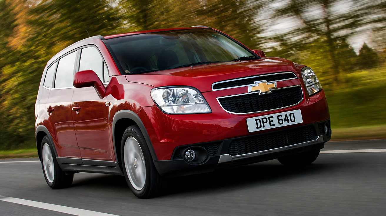 Roter Chevrolet SUV fährt auf einer Straße mit verschwommenem Wald im Hintergrund.