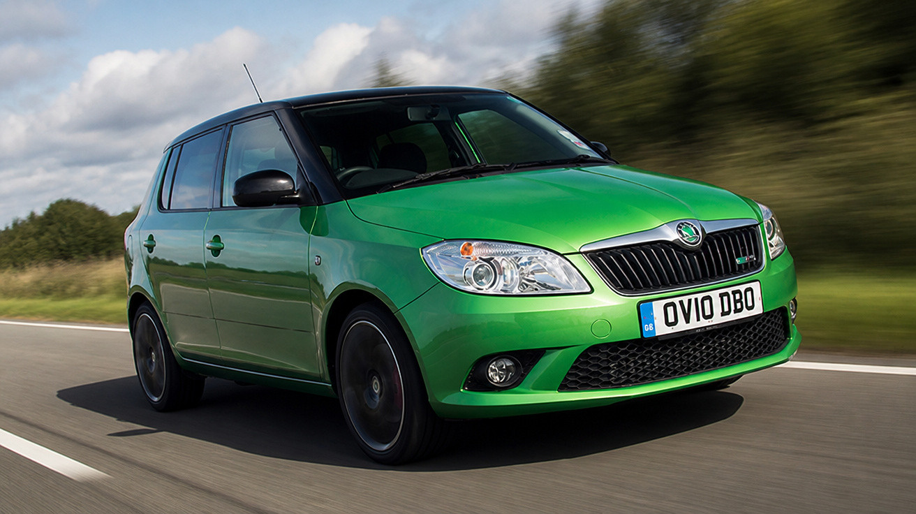 Grüner Skoda Fabia fährt auf Landstraße bei bewölktem Himmel, grüne Landschaft im Hintergrund.