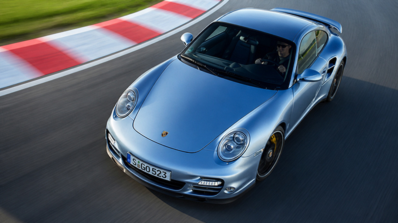 Silberner Porsche 911 auf Rennstrecke, schnelle Kurvenfahrt mit Fahrer im Fahrzeug.
