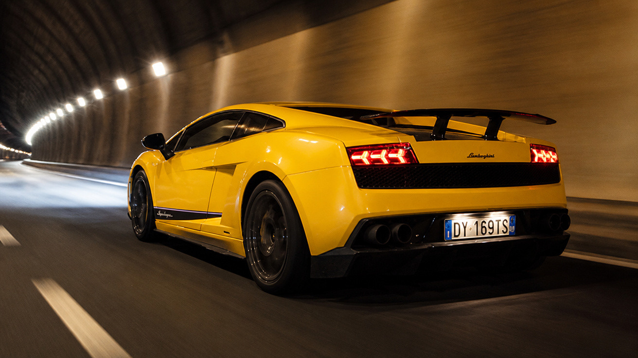 Gelber Lamborghini-Sportwagen fährt in beleuchtetem Tunnel, seitliche Rückansicht bei Nacht.