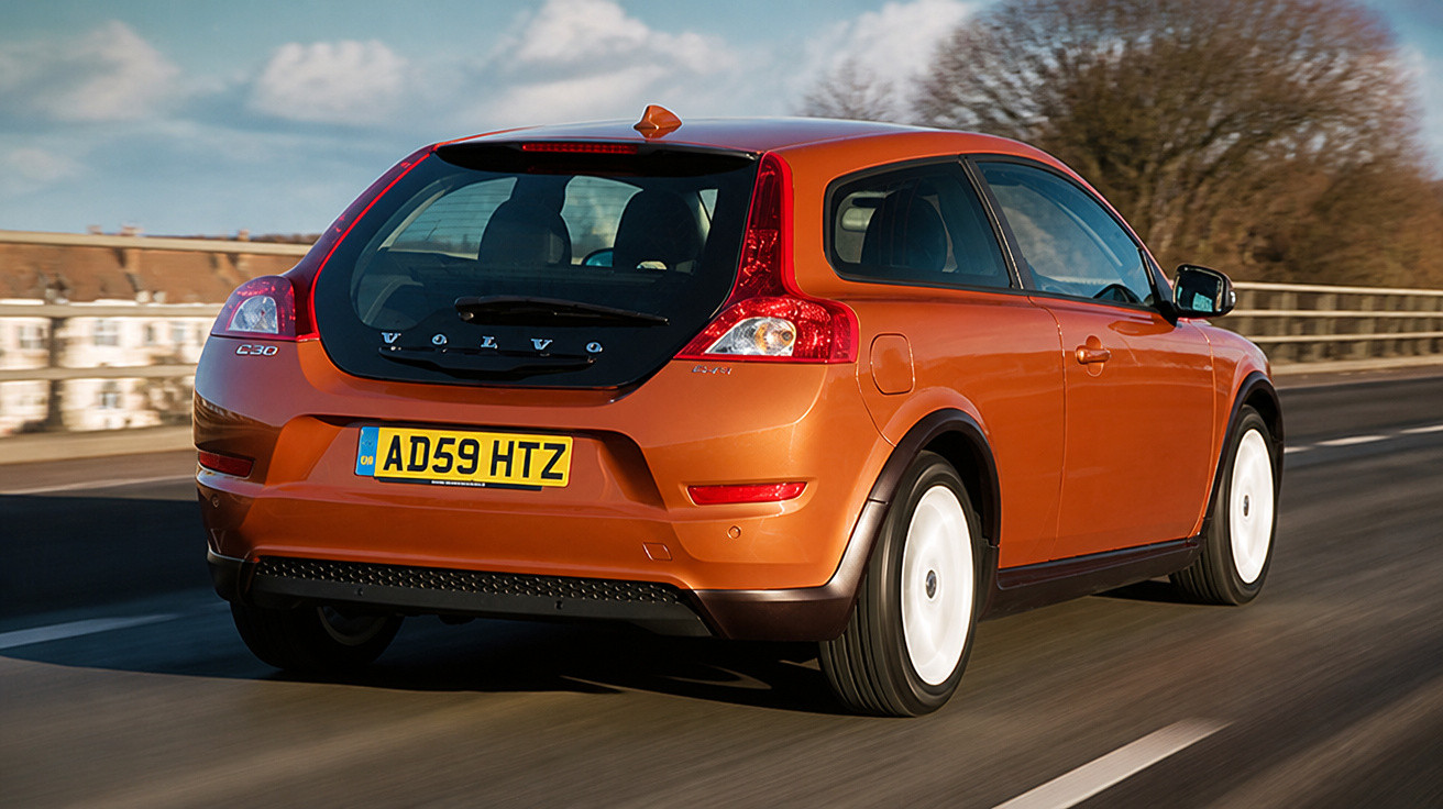 Orangefarbener Volvo C30 fährt auf einer Straße bei klarem Himmel, Rückansicht.