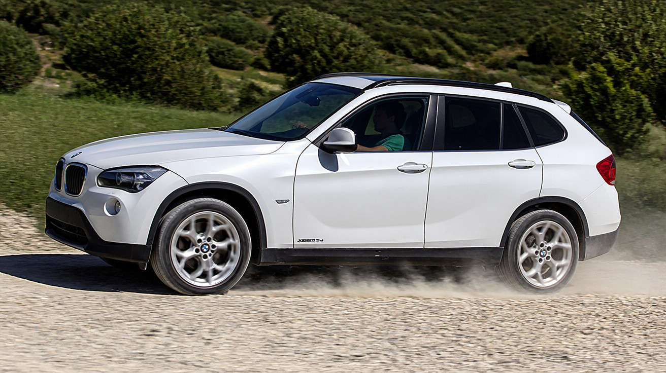 Weißer BMW SUV fährt auf einer unbefestigten Straße in ländlicher, grüner Umgebung.