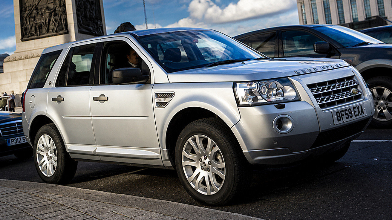 Silberner Land Rover SUV, geparkt an einer Straße bei Tageslicht mit Gebäuden im Hintergrund.