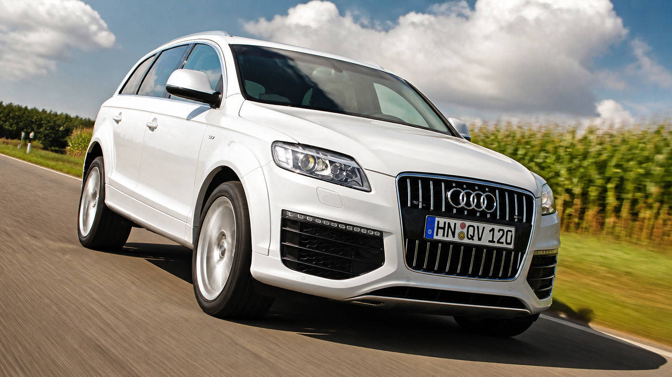 Weißer Audi SUV fährt auf Landstraße bei sonnigem Wetter mit blauem Himmel und Wolken.