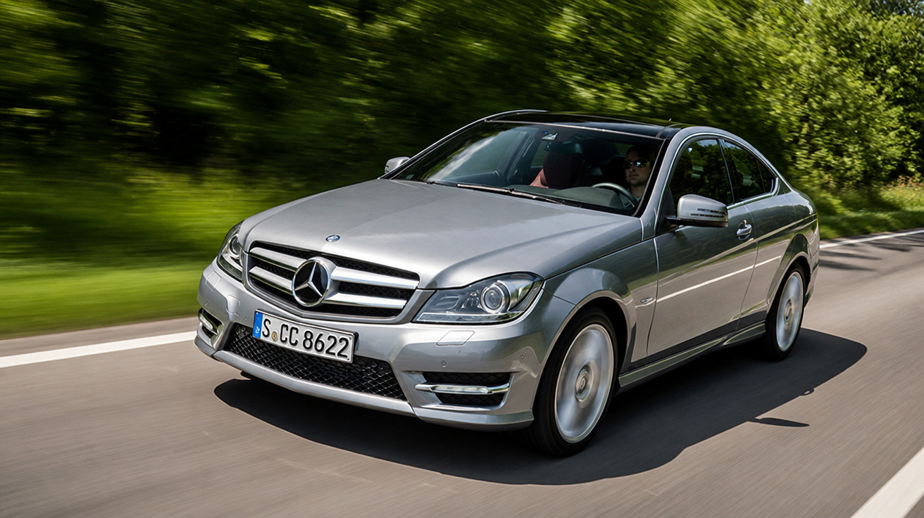 Silberner Mercedes-Benz der C-Klasse fährt dynamisch auf Landstraße mit grünem Wald im Hintergrund.
