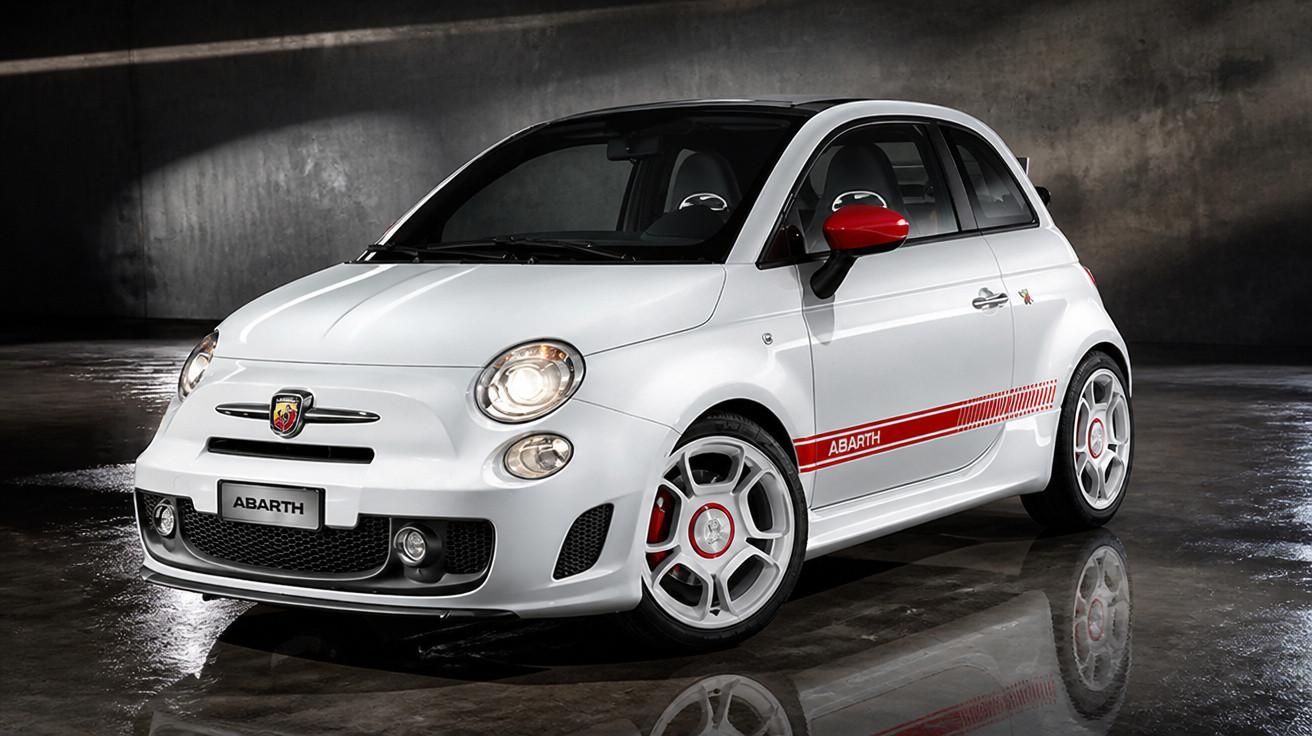 Weißer Abarth Kleinwagen mit roten Details vor dunklem, nassem Betonboden in Studioaufnahme.